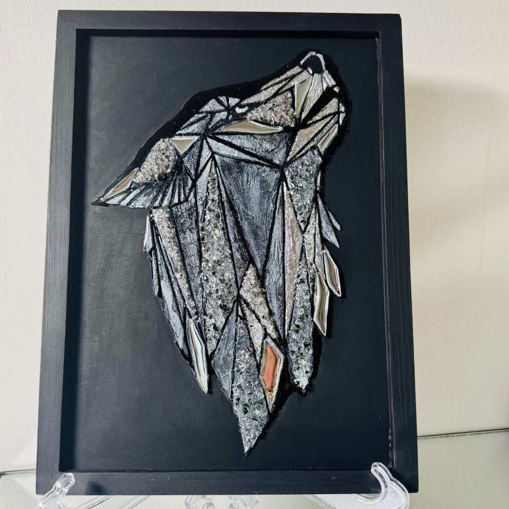 Ein grafisches, schimmerndes Bild eines Wolfskopfes auf mattschwarzem Hintergrund. Das Bild besteht aus handgeschnittenen, spiegelnden Dreieckselementen, strukturierter Paste, die mit schimmernder Farbe bemalt wurde, und spiegelnden Kristallen, die die Leuchtkraft des Gemäldes verstärken. Das Wolfsbild ist mit Epoxidharz überzogen, wodurch die zentrale Komposition mit dem Licht spielt und dem Betrachter aufregende Momente schenkt. Dadurch lässt sich das Gemälde auch berühren und haptisch erleben